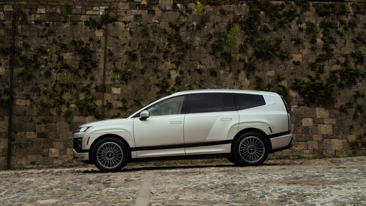White luxury SUV parked against stone wall with ivy, featuring distinctive multi-spoke wheels