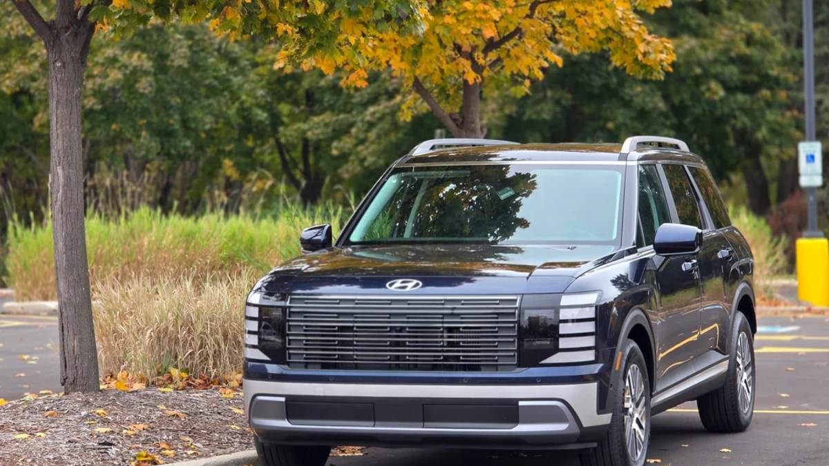 2026 Hyundai Palisade in black, front three-quarter view, featuring distinctive horizontal grille design and LED lighting, parked under autumn trees.