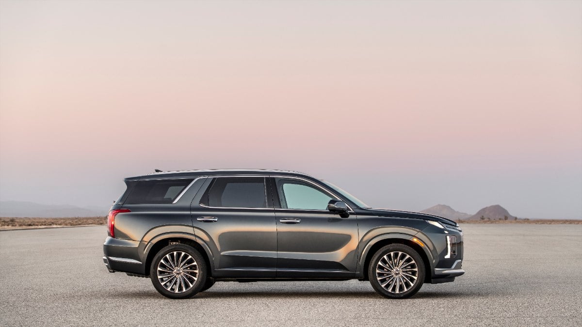 Dark gray 2026 Hyundai Palisade SUV parked on desert ground with soft sunset sky, side profile view with sleek design and multi-spoke wheels