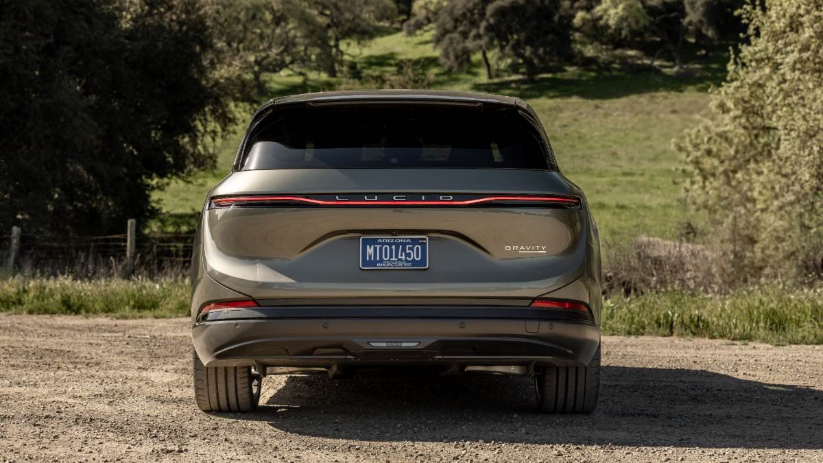 Rear view of a Lucid Gravity SUV parked on a dirt road with grassy hills behind.