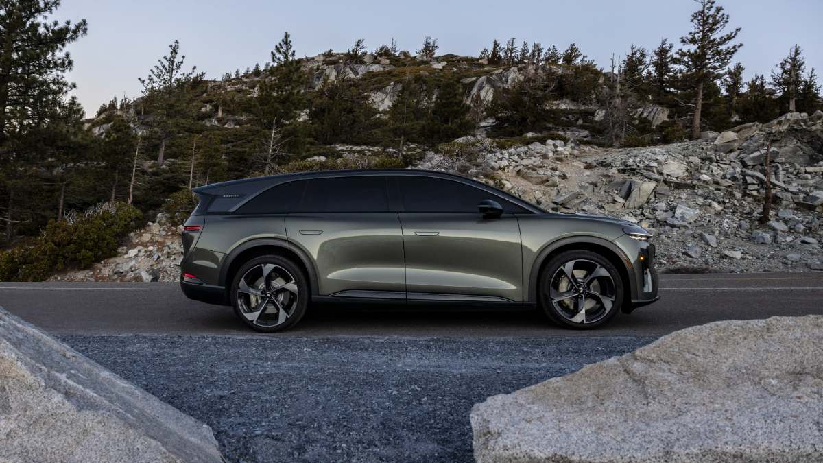 2026 Lucid Gravity SUV in metallic sage green, side profile view, featuring black contrast roof and sporty wheels, photographed on mountain road with rocky terrain.