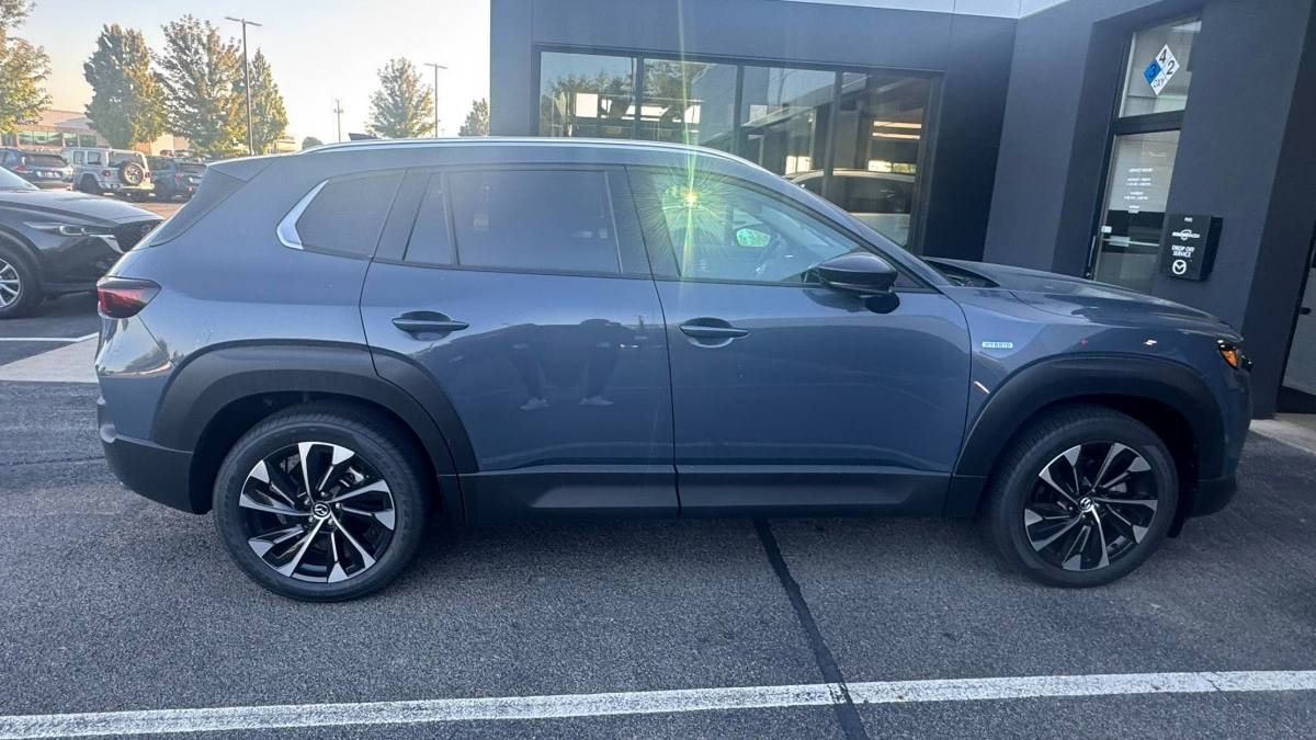 2026 Mazda CX-50 in metallic blue, side profile view, featuring black trim, distinctive two-tone alloy wheels, parked outside dealership.