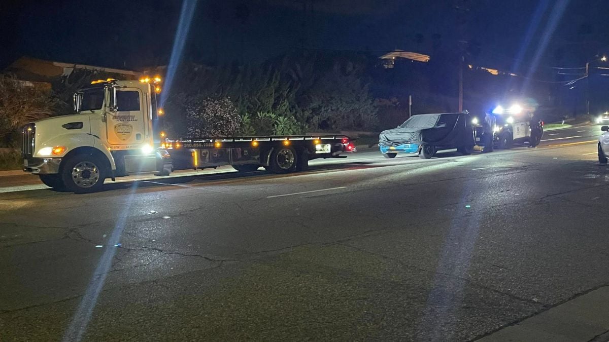 2026 Rivian R2 electric SUV prototype front three-quarter view being loaded onto a tow truck at night with police lights visible.