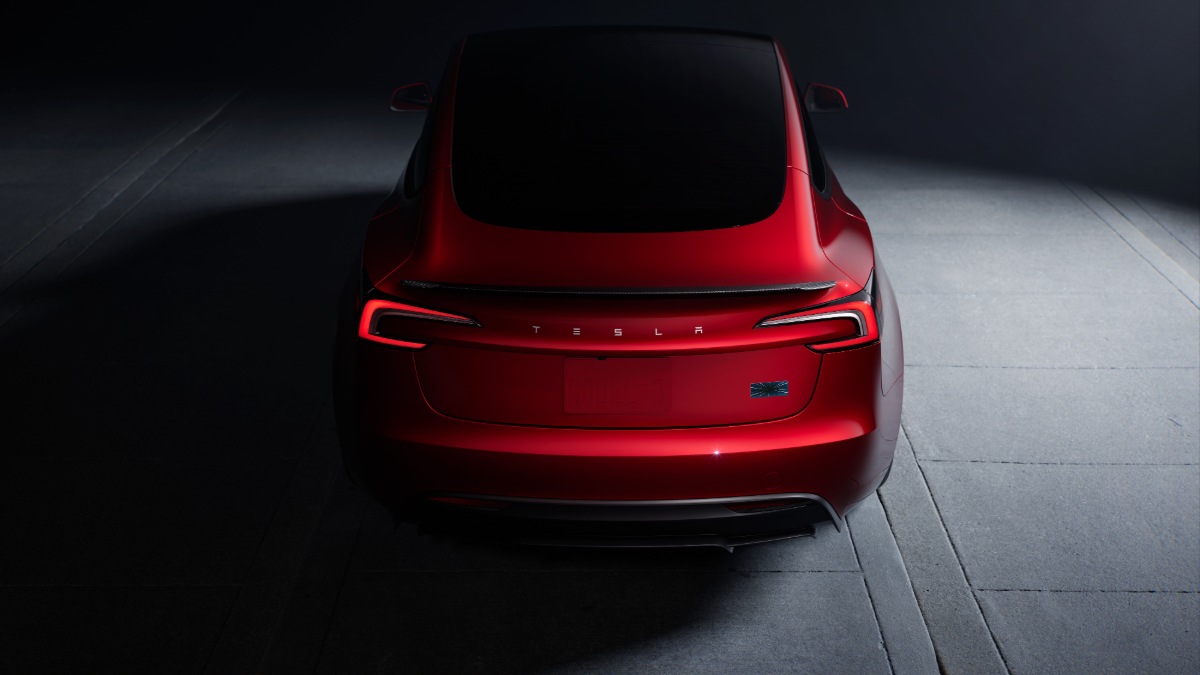 Rear view of a red Tesla car parked on a concrete surface, illuminated by overhead light.