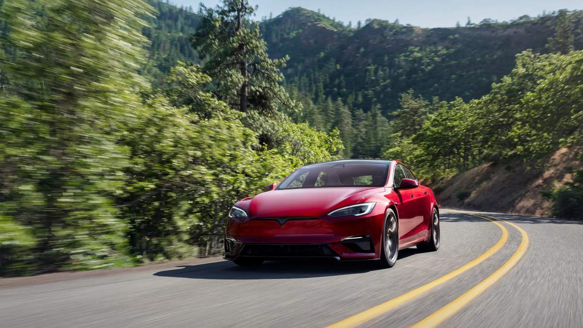 Red car driving on a winding road through a forested mountainous area.