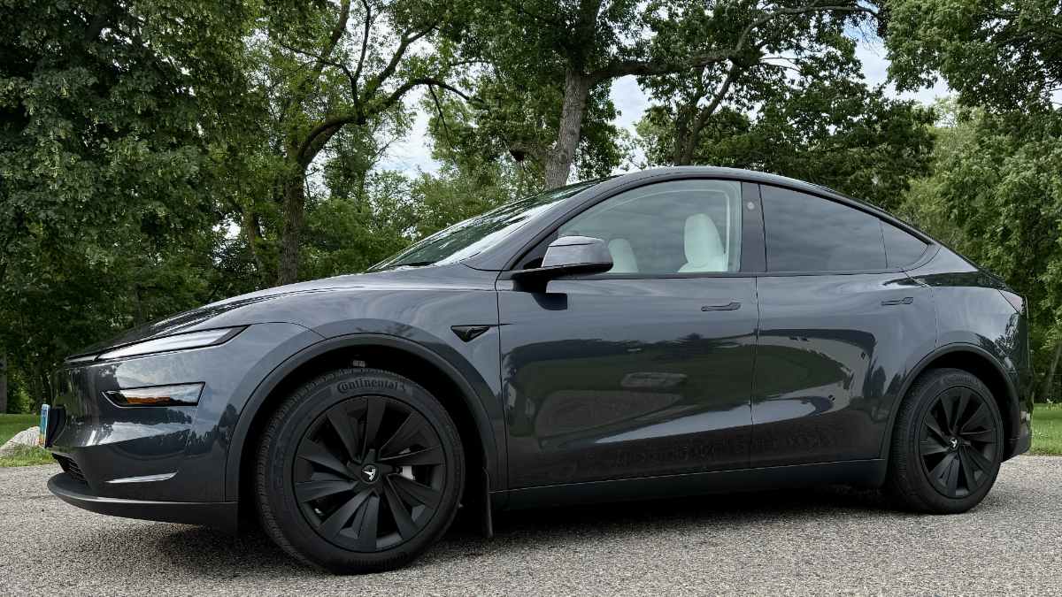 Dark gray Tesla Model Y side profile parked on pavement with trees in the background.
