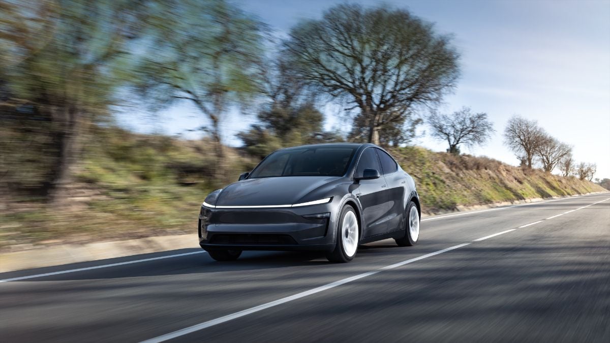 Black Tesla Model Y driving on rural highway with blurred trees and blue sky background