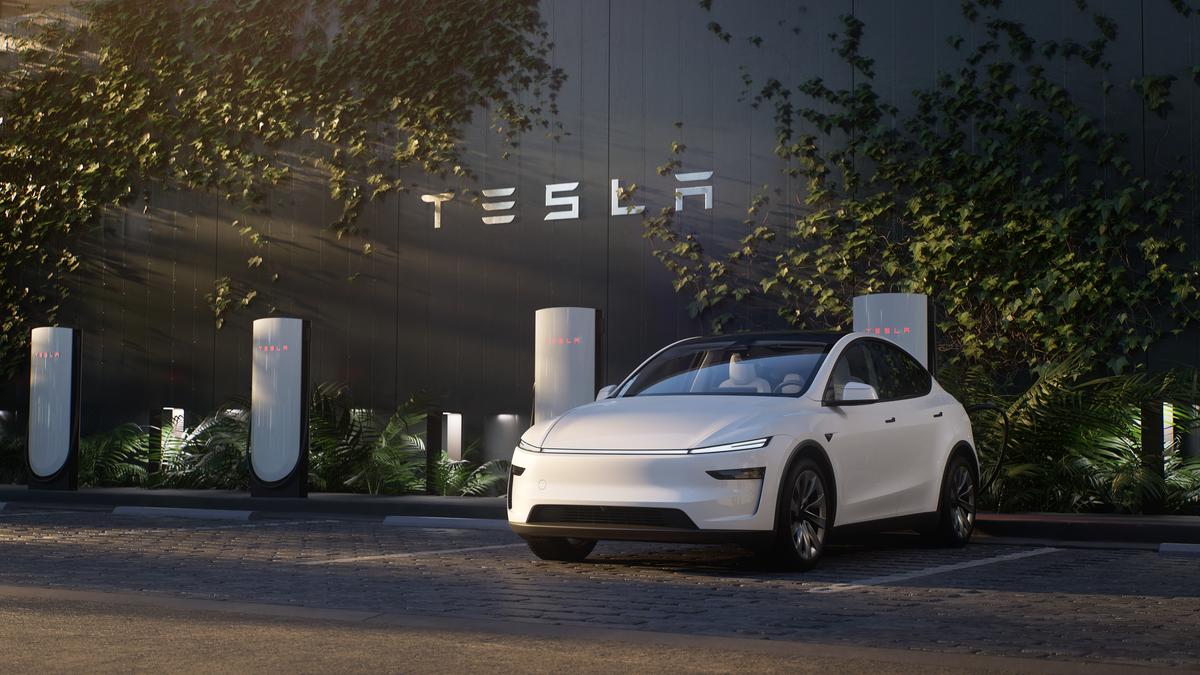 Photograph of a 2026 Tesla Model Y electric vehicle in the Juniper White color, shown from a front 3/4 angle with the Tesla logo and text visible in the background.