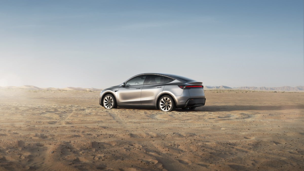 Silver electric car parked on a sandy desert landscape under a clear blue sky.