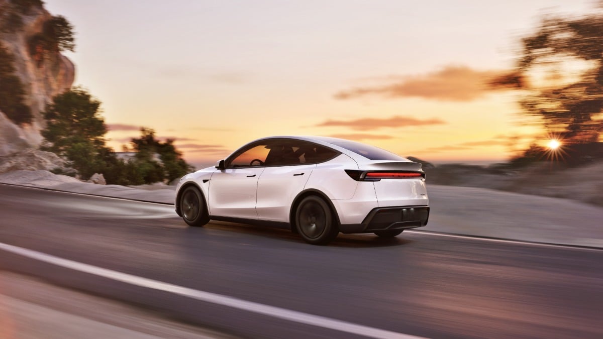 2026 Tesla Model Y Juniper in white driving on a mountain road at sunset, rear three-quarter view showcasing updated taillight bar and aerodynamic fastback design.