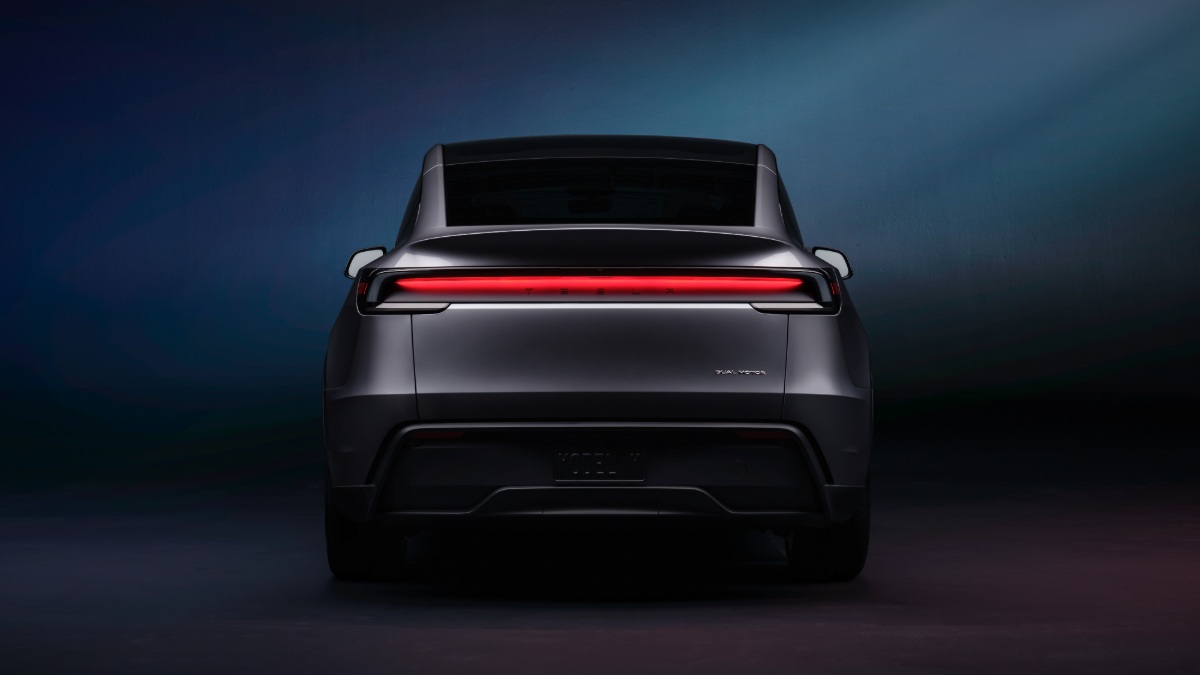 2026 Tesla Model Y Juniper in gray shown from the rear, featuring full-width LED taillight bar and refreshed bumper styling in studio lighting.