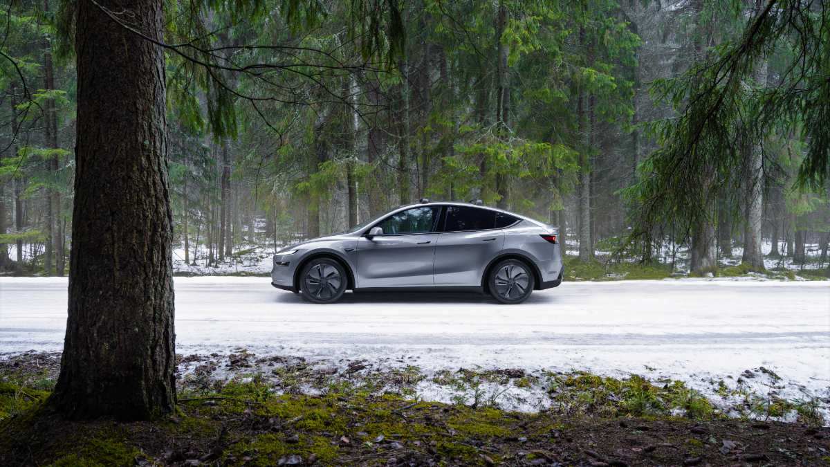 2026 Tesla Model Y in gray, side view, parked on snowy ground with trees in the background.