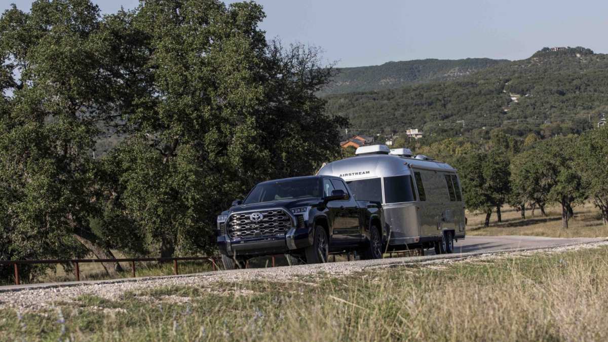 Truck towing an Airstream trailer on a rural road with trees and hills in the background.