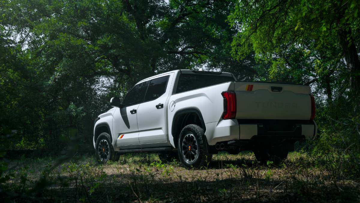 A white 2026 Toyota Tundra pickup truck shown from the rear three-quarter view, positioned in a wooded setting with dramatic lighting highlighting its modern body lines and black accents.