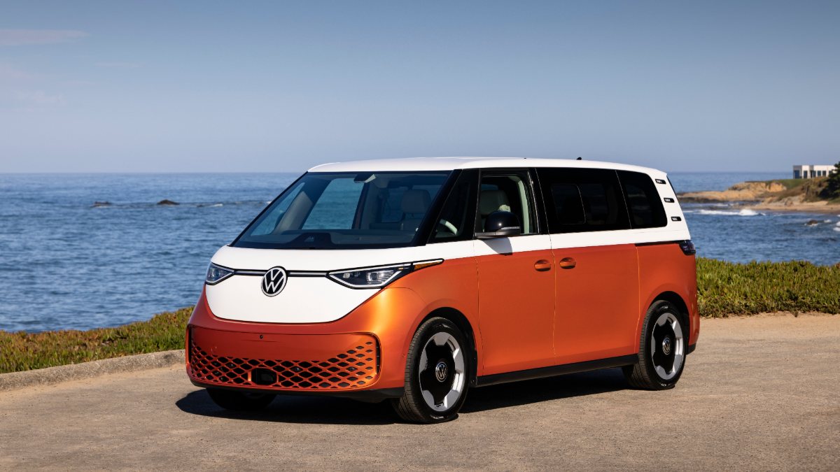 Orange and white Volkswagen ID. Buzz electric van parked on coastal cliff overlooking ocean.