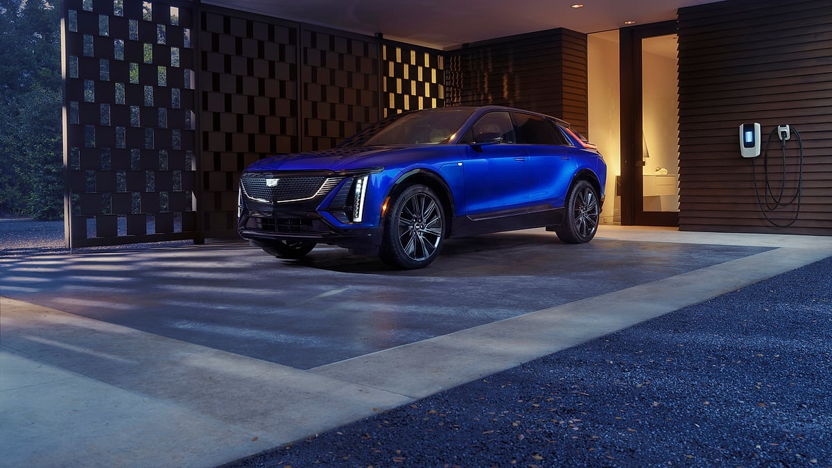 Blue 2026 Cadillac Lyriq parked under a modern carport next to a home EV charger.