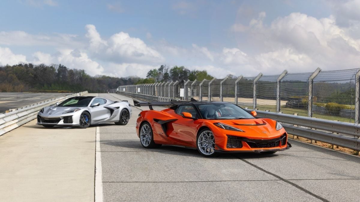 Orange and silver Chevrolet Corvette C8 convertibles parked on a racetrack with safety barriers behind them.