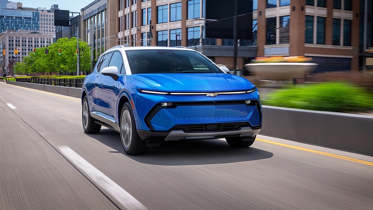 Blue 2026 Chevrolet Equinox EV LT driving on an urban road with buildings in the background.