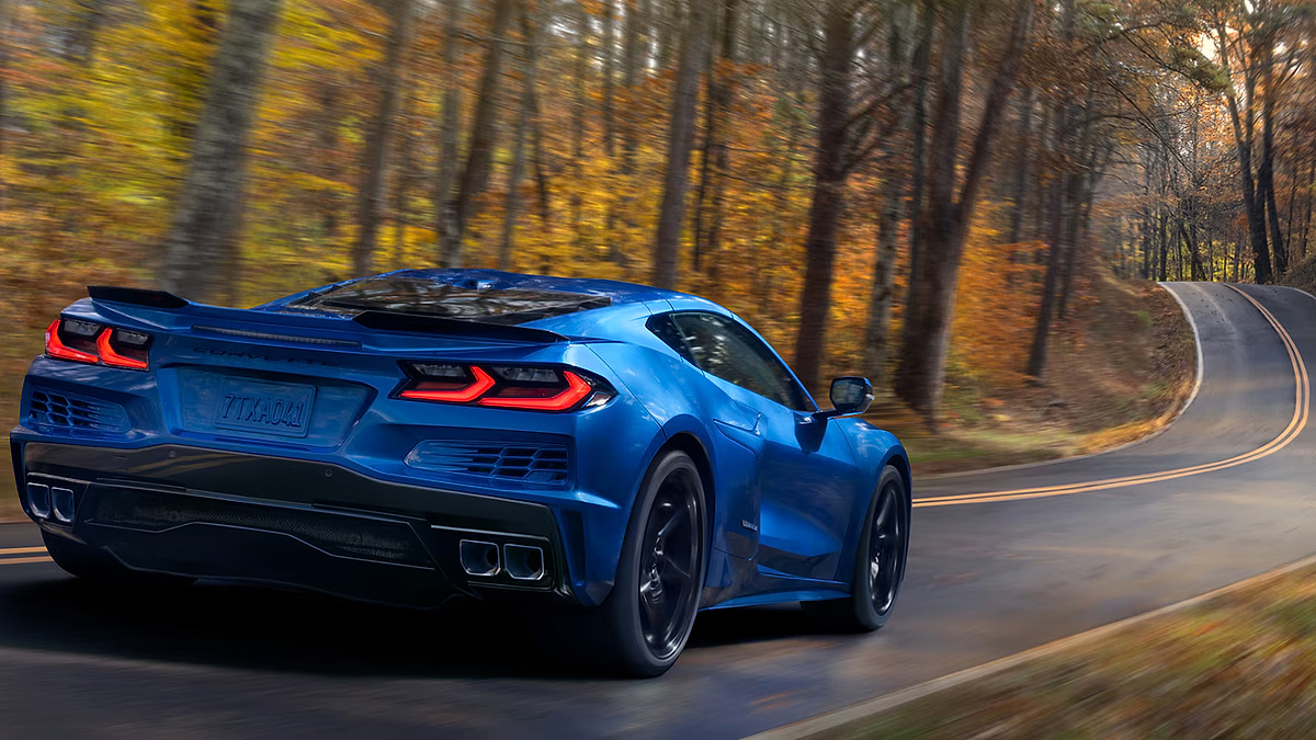 Blue Chevrolet Corvette C8 driving on curvy road through autumn forest