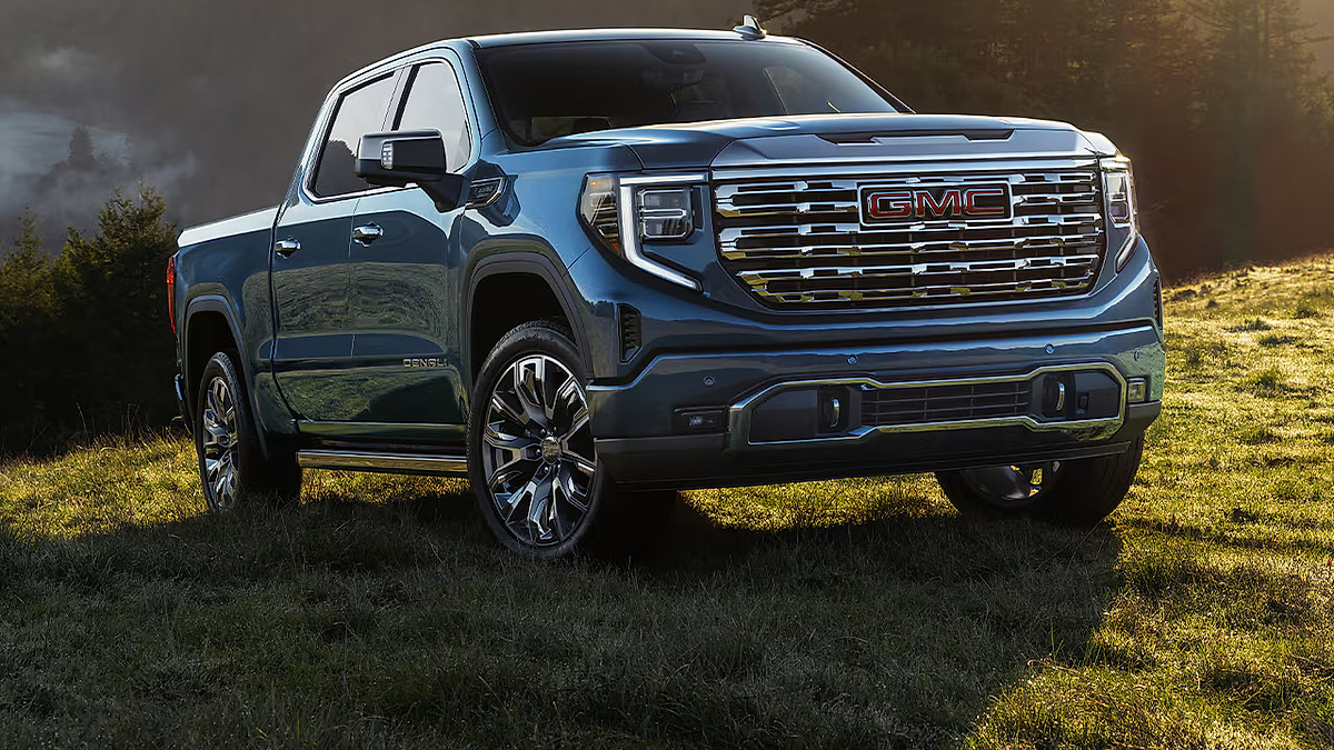 Blue 2026 GMC Sierra 1500 Denali parked on a grassy field, shown from the front three-quarter angle.