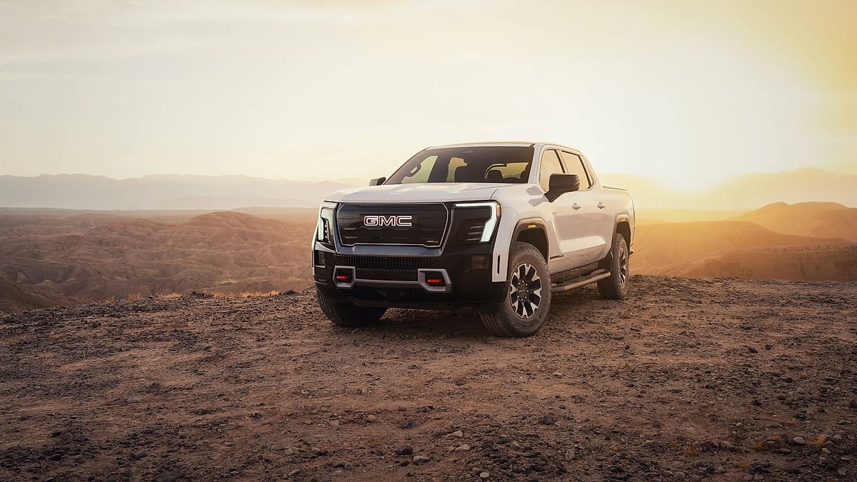 White 2026 GMC Sierra EV AT4 parked on rocky desert terrain during golden-hour light.