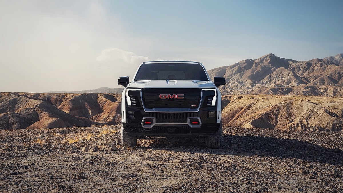 White 2026 GMC Sierra EV AT4 parked at a desert canyon overlook with the truck bed facing the camera.