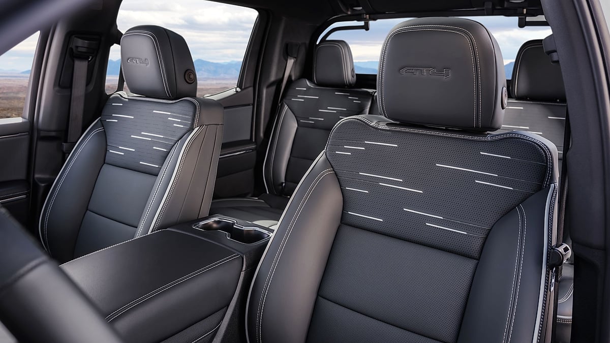 Front-seat interior detail of the 2026 GMC Sierra EV AT4 showing black seats with AT4 logos, contrast stitching, and patterned seat inserts.