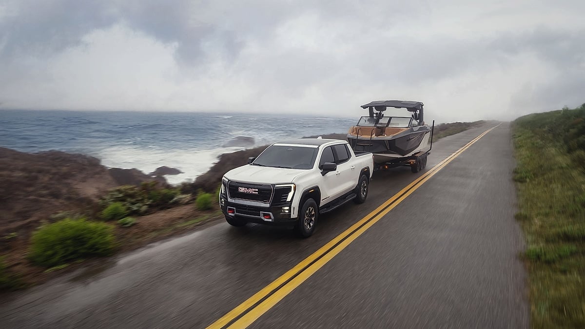 White 2026 GMC Sierra EV AT4 towing a boat along a foggy coastal road.