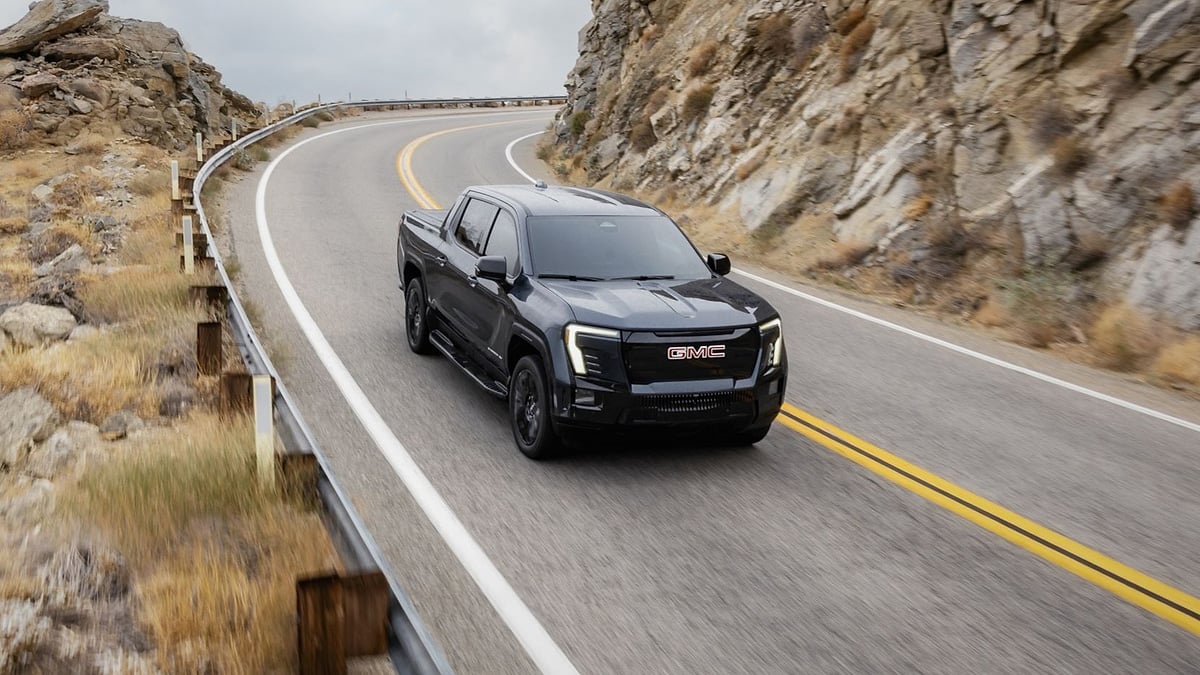 Black 2026 GMC Sierra EV Elevation driving on a winding mountain road in a front three-quarter view.