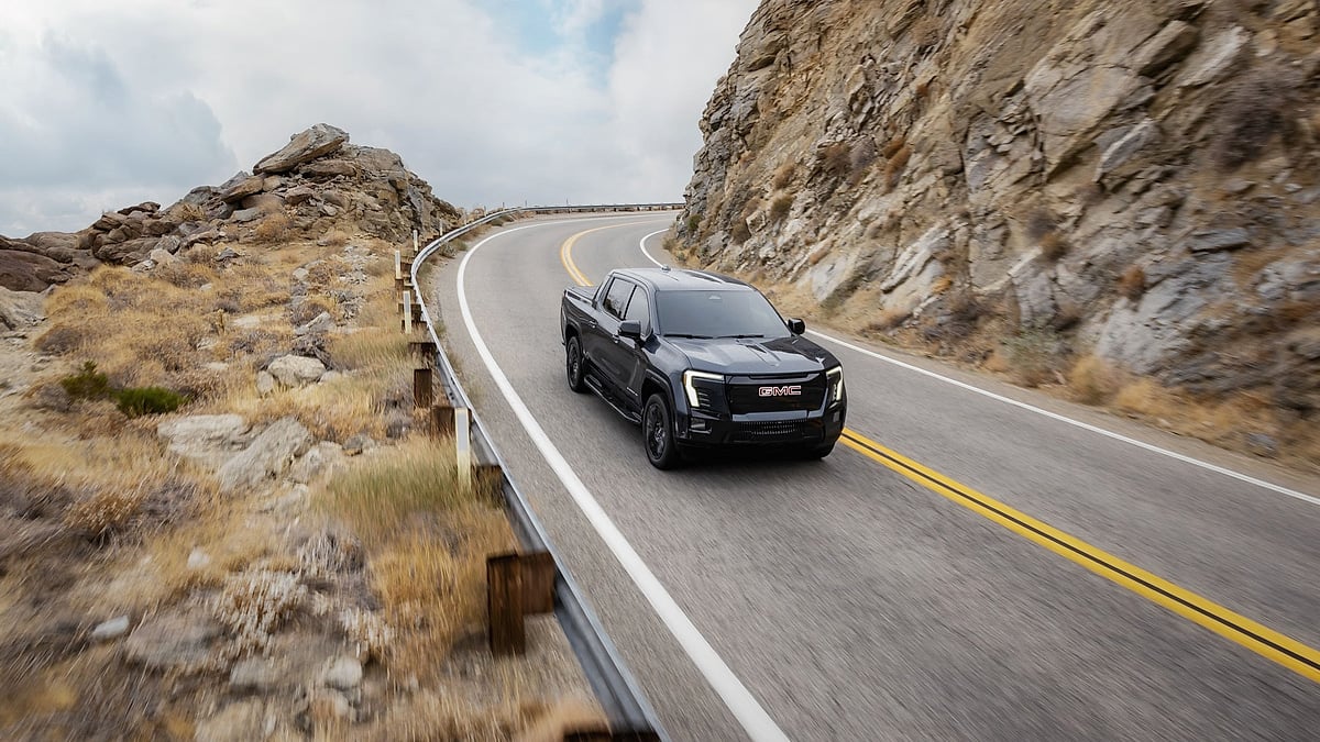 Black 2026 GMC Sierra EV Elevation driving on a winding mountain road in a front action view.