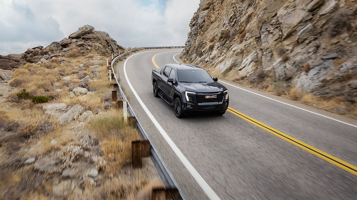 Black 2026 GMC Sierra EV Elevation driving on a winding mountain road between rocky canyon walls.