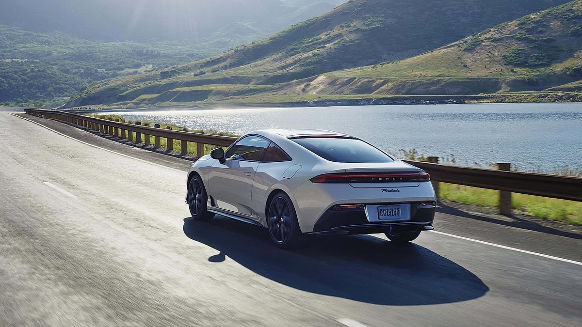 2026 Honda Prelude hybrid coupe in white driving along a scenic coastal highway with lake and green hills in background