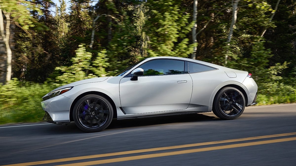 2026 Honda Prelude hybrid coupe in silver side profile view driving through a lush green forest road with motion blur