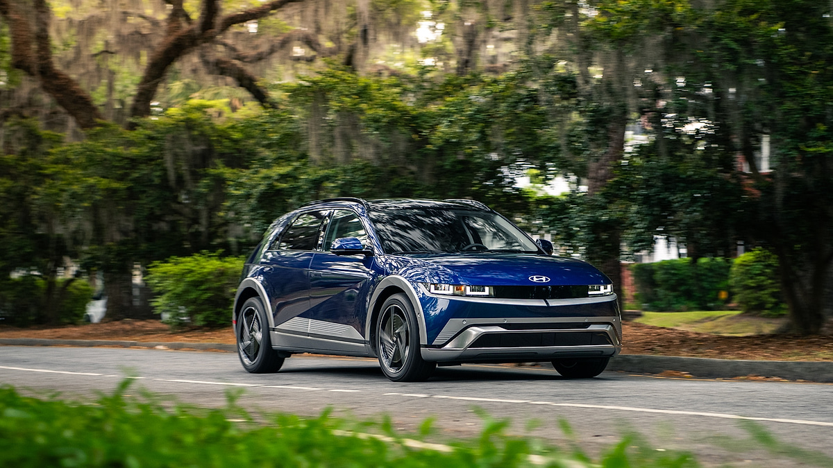 Blue 2026 Hyundai Ioniq 5 driving along a tree-lined road.