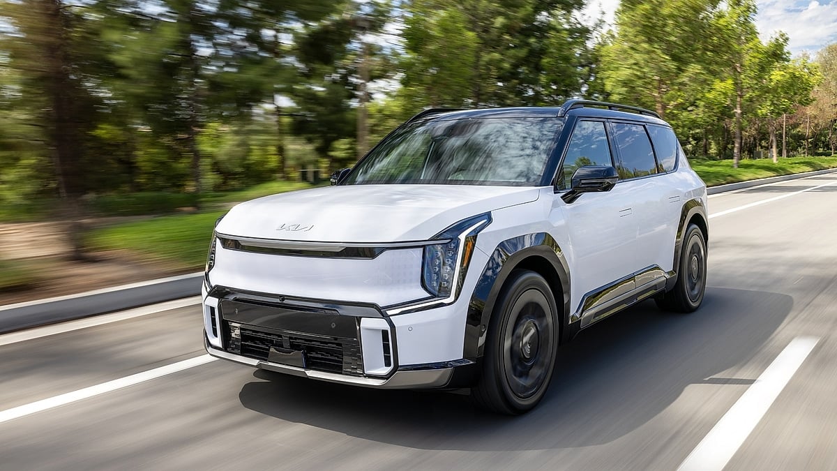 2026 Kia EV9 electric SUV in white driving on a highway, front three-quarter view