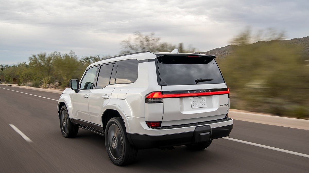 White Lexus GX driving on a desert road, shown from the rear three-quarter angle.