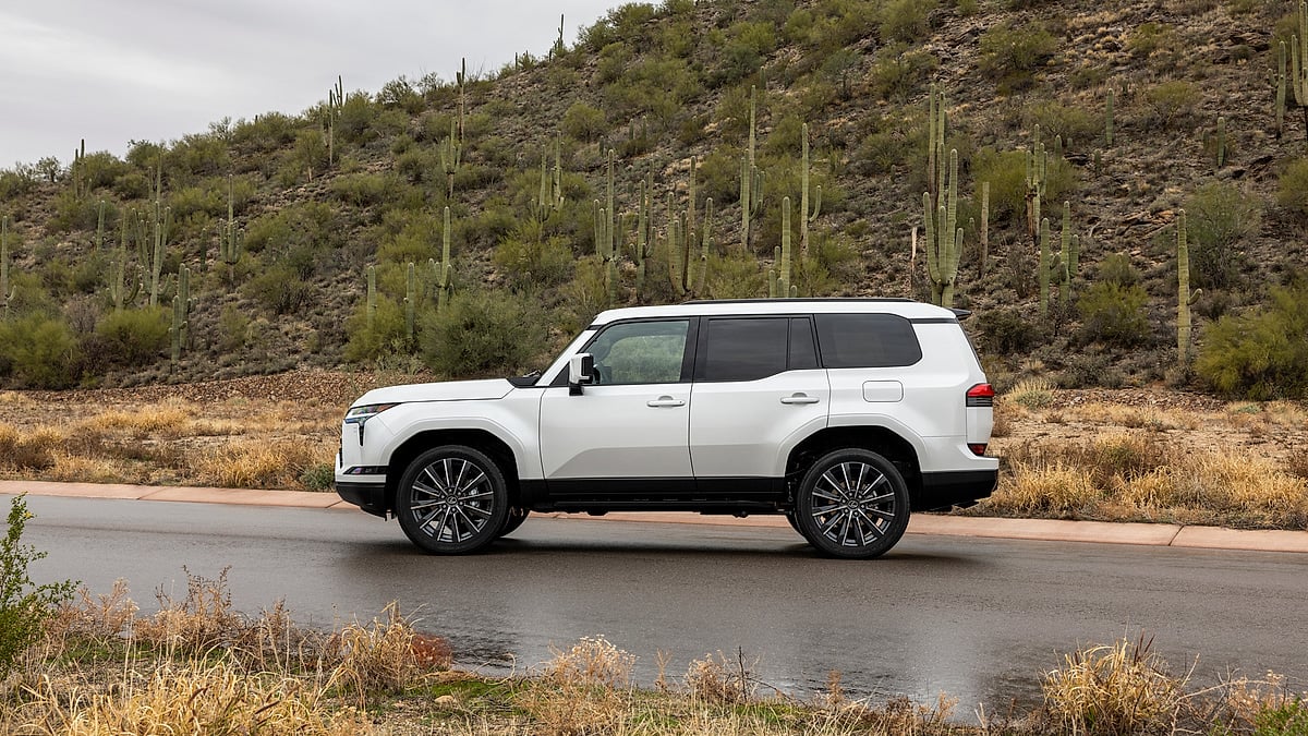 White Lexus GX parked in profile beside a desert hillside filled with cactus plants.