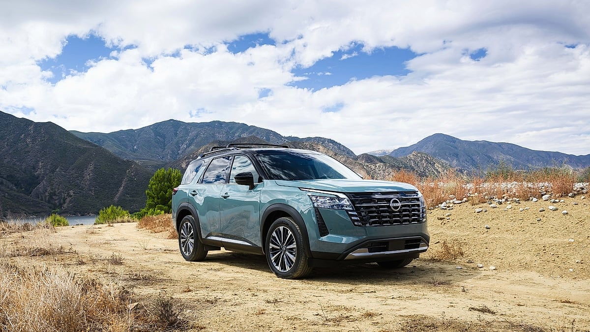Light blue 2026 Nissan Pathfinder SUV parked on a dirt overlook with mountains in the background.