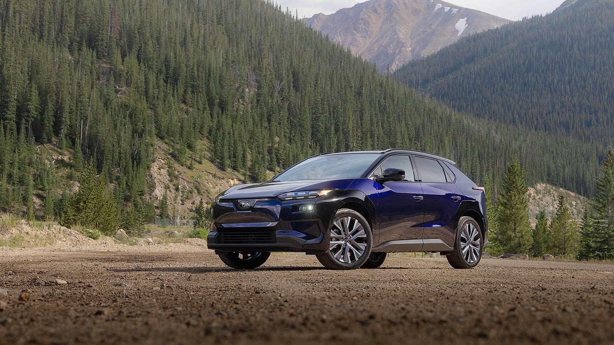 Blue 2026 Subaru Solterra parked on a dirt overlook with forested mountains in the background.