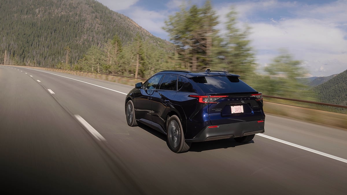 Blue 2026 Subaru Solterra driving on a mountain highway in a rear three-quarter action view.