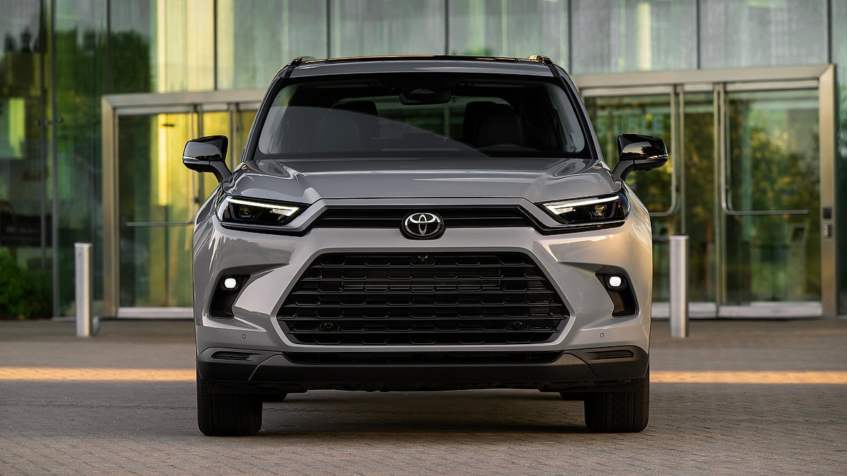 Cement gray 2026 Toyota Grand Highlander Nightshade shown from the front outside a modern glass building.
