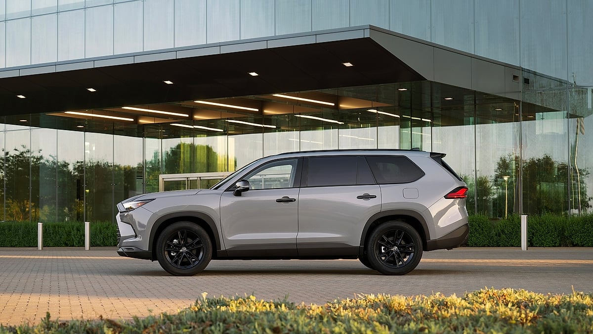Cement gray 2026 Toyota Grand Highlander Nightshade shown in side profile outside a modern glass building.