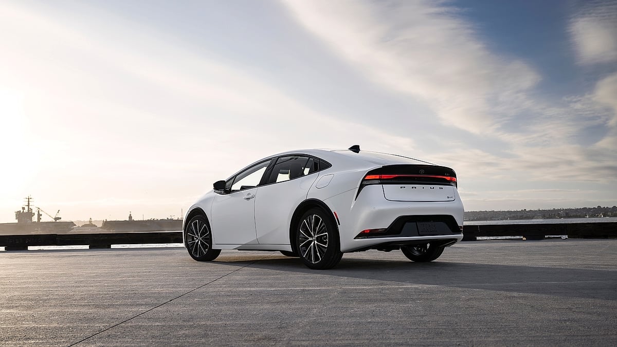 White 2026 Toyota Prius Limited parked by the waterfront, shown from the rear three-quarter angle with the city shoreline in the distance.