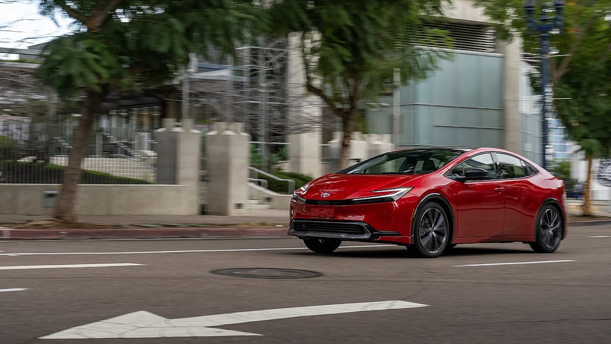 Red 2026 Toyota Prius XLE driving on an urban street with buildings and trees blurred in the background.