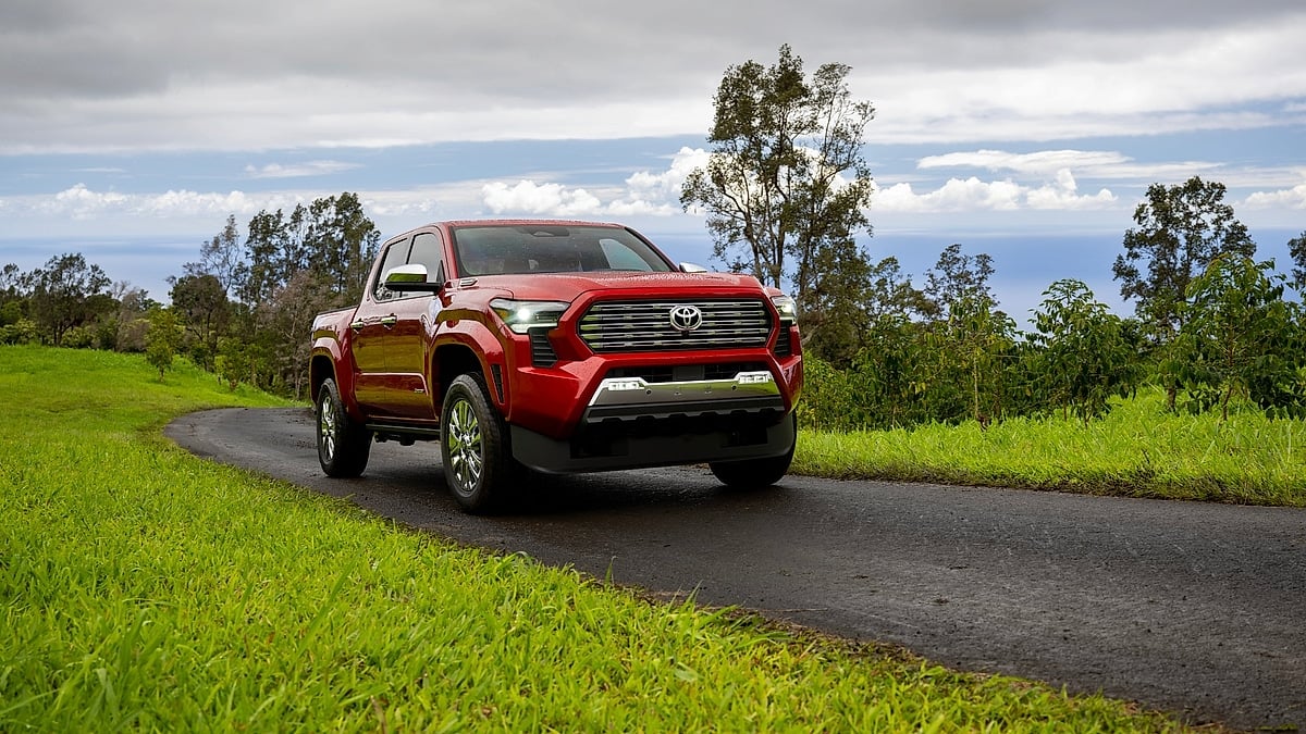 Red 2026 Toyota Tacoma Limited driving on a narrow paved road through green hills near the ocean.