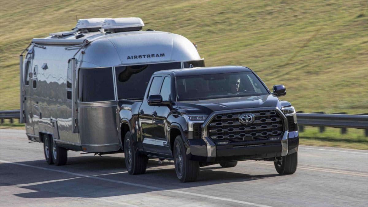 Black 2026 Toyota Tundra TRD Platinum towing silver Airstream trailer on highway with grassy hills
