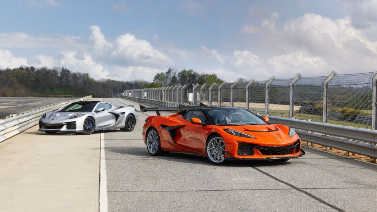 Orange and silver Chevrolet Corvette C8 ZR1X sports cars parked on a racetrack, front three-quarter view showcasing high-performance aero, wide stance, and track-focused design.