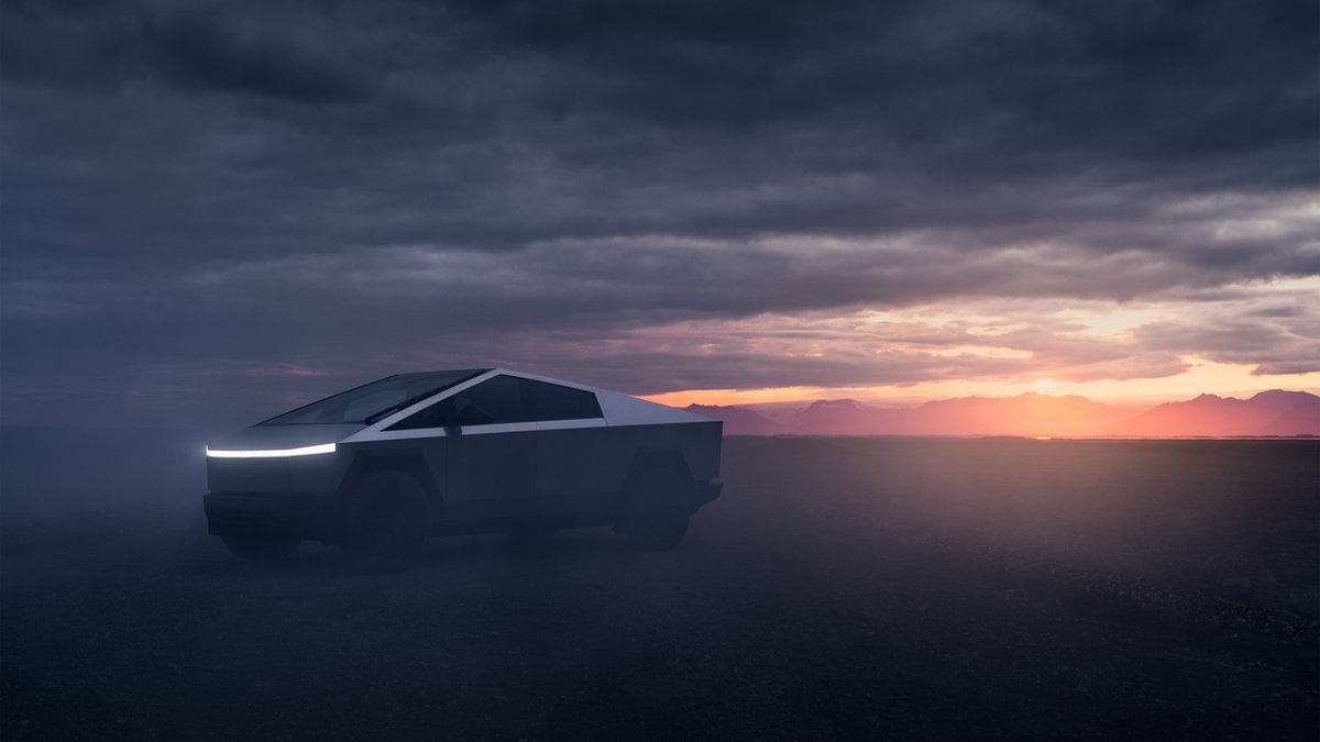 The Tesla Cybertruck's distinctive angular silhouette is shown in a dramatic side profile against a dusky sunset sky, with its signature LED light bar prominently illuminated in the darkness.