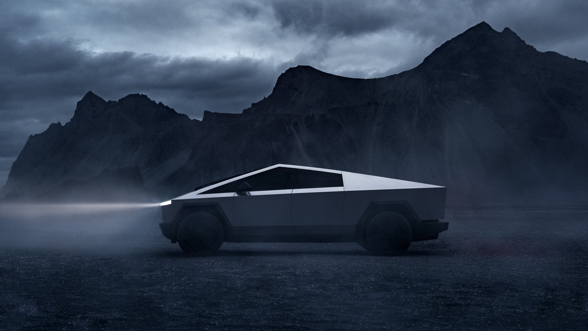 Tesla Cybertruck stainless steel exterior shown in side profile parked in a misty mountain landscape.