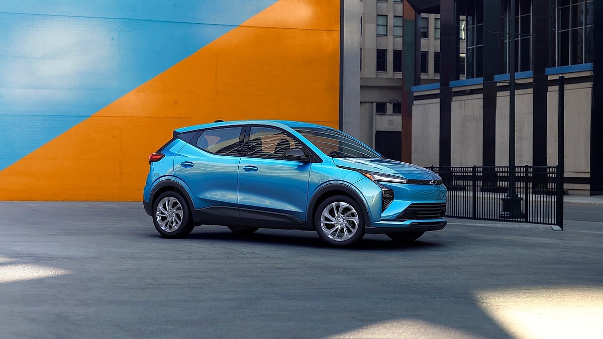 Blue 2027 Chevrolet Bolt shown from the passenger side near a colorful urban mural.